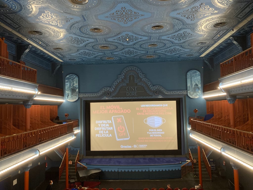 Interior del Cine Doré en Madrid con pantalla y platea iluminadas durante una sesión