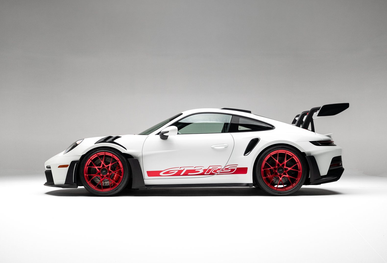 Side-profile studio view of the white 2023 Porsche 911 GT3 RS with red wheels, GT3 RS graphics, and rear wing.