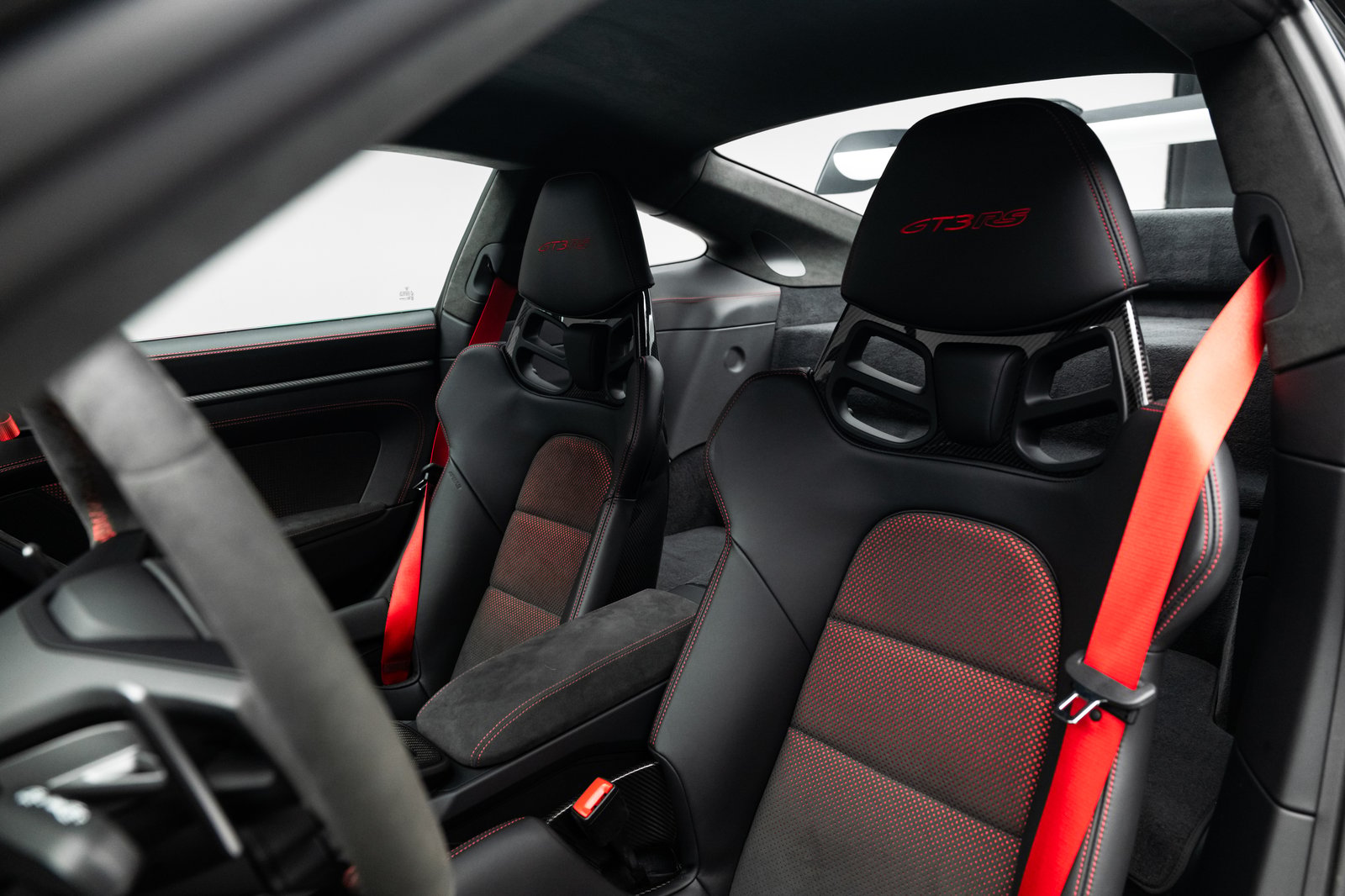 Interior view of the 2023 Porsche 911 GT3 RS showing black carbon-fiber bucket seats with red seat belts and red upholstery accents.