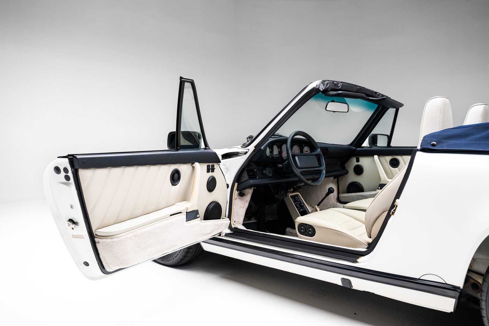Pearl White leather interior of the 1988 Porsche 911 Carrera Cabriolet with the manual shifter and black dashboard visible.