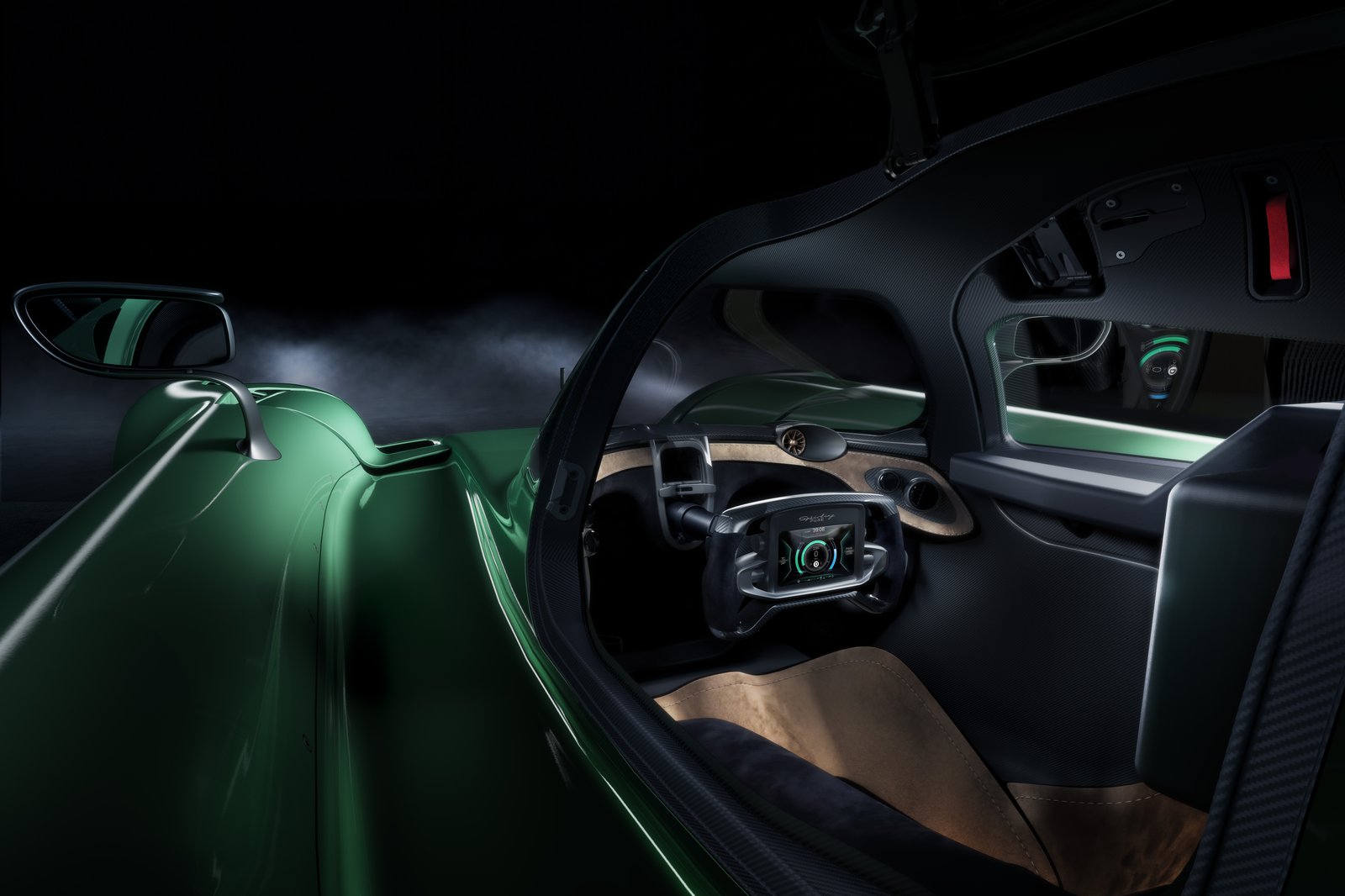 A green open-cockpit sports car is shown in a dark studio setting with the canopy/door area open, revealing the driver-focused interior. Visible details include carbon-fiber trim, a compact steering wheel with a digital display, a side mirror, and sculpted bodywork.