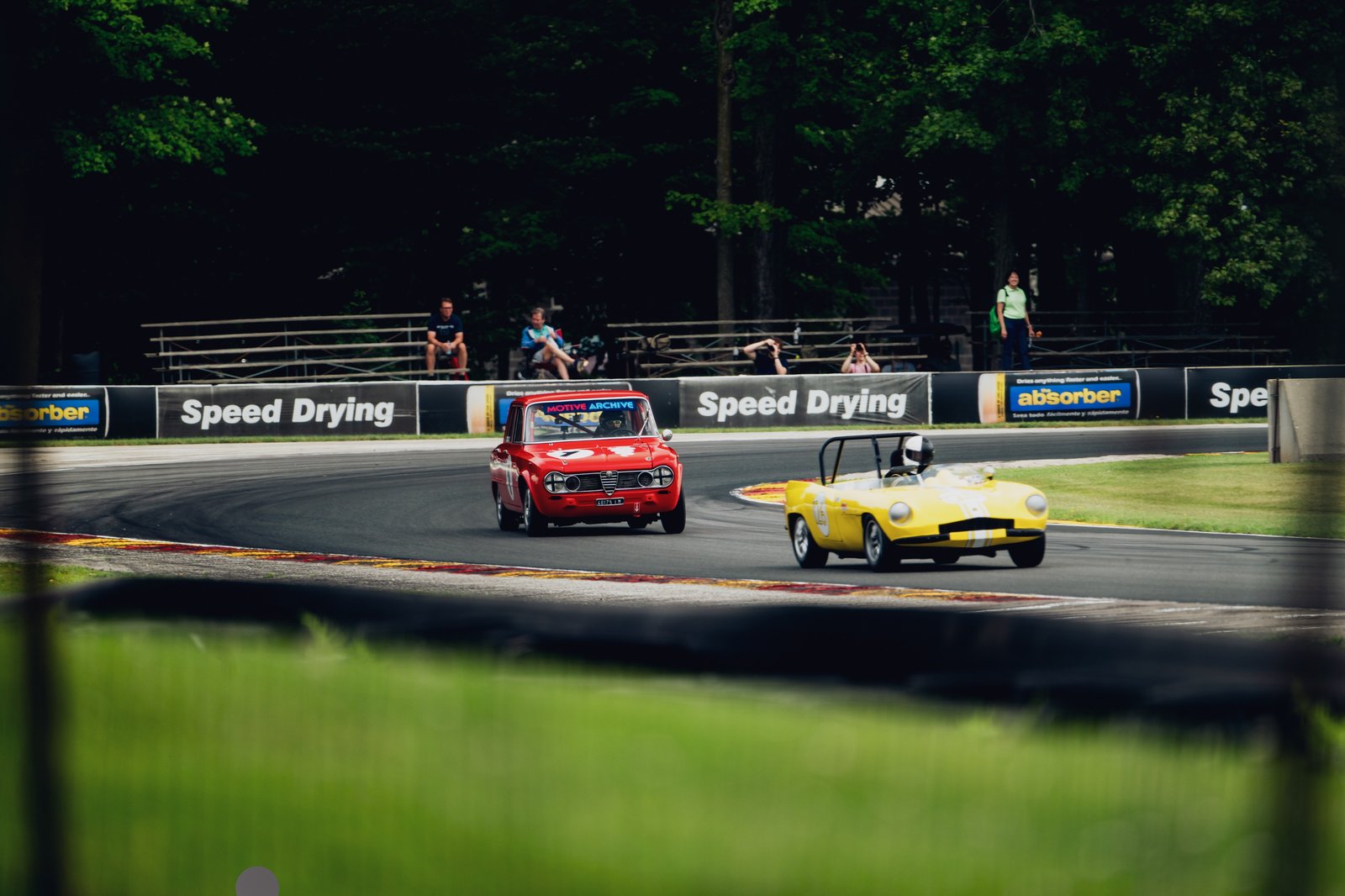 Two racing cars, one red and one yellow, captured from a front 3/4 angle on a curved track during a motorsport event.