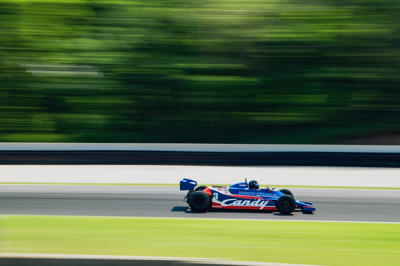 Racing car in motion on a racetrack, side view, showcasing vibrant design and blurred background.