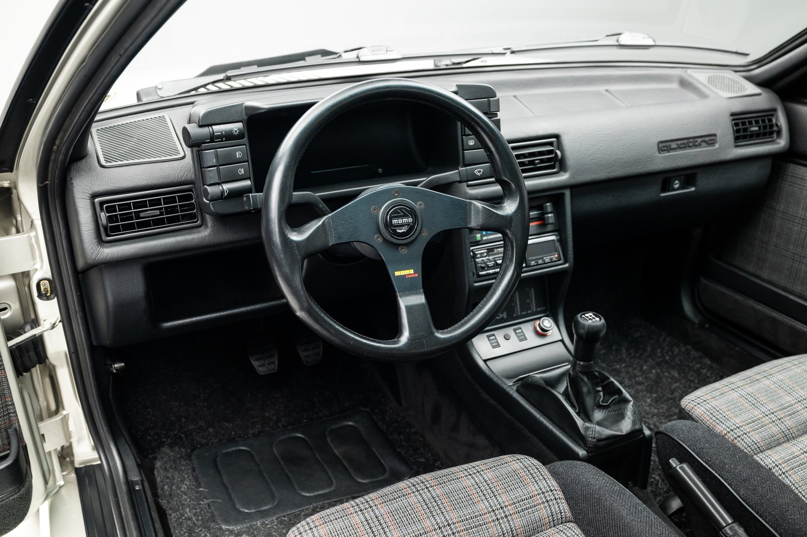 Cockpit view showing the steering wheel, dashboard, shifter, and plaid seats.