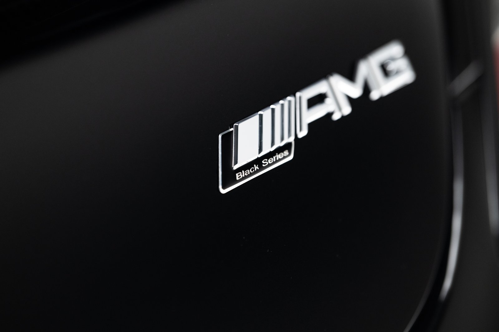 Close-up detail of an AMG Black Series badge on a black vehicle body panel. The image has shallow depth of field with the badge centered against glossy dark paint.