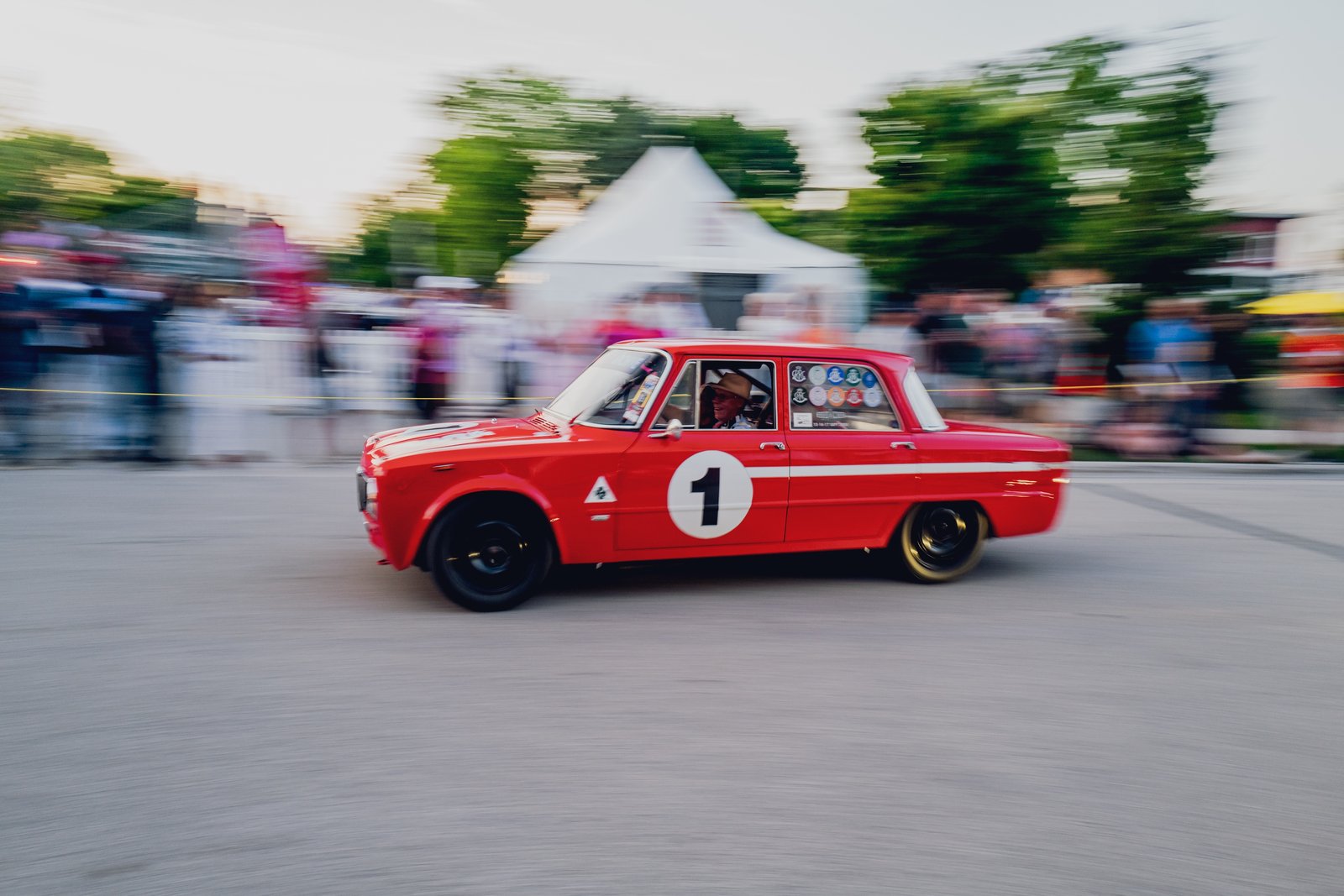 Red vintage car in front 3/4 view, number '1', in motion at sunset during a vintage racing event.