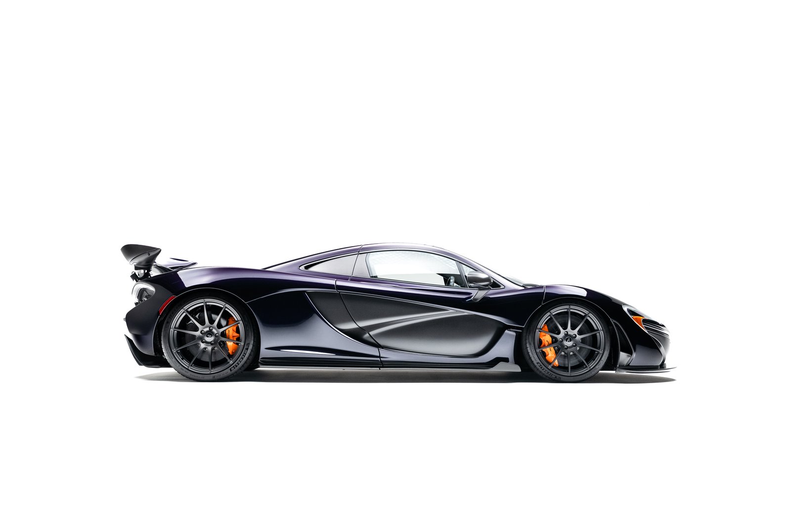 Side profile exterior shot of a 2015 McLaren P1 in Amethyst Black on a white background, showing carbon side intakes, rear wing, and orange calipers.