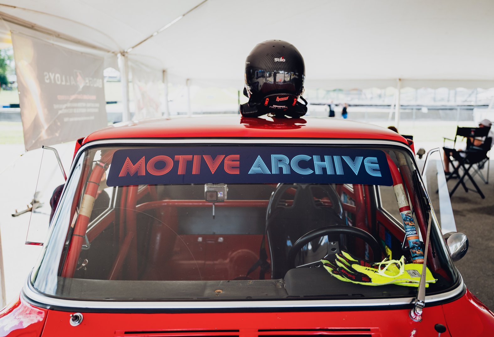 View of a red car featuring a roll cage, helmet on roof, and gloves on the dashboard.