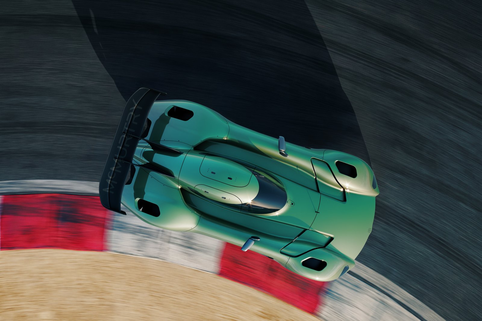 An overhead exterior shot shows a green track-focused sports car on a racetrack curb. The car has a large rear wing, roof scoop, aerodynamic vents, and motion-blurred pavement around it.