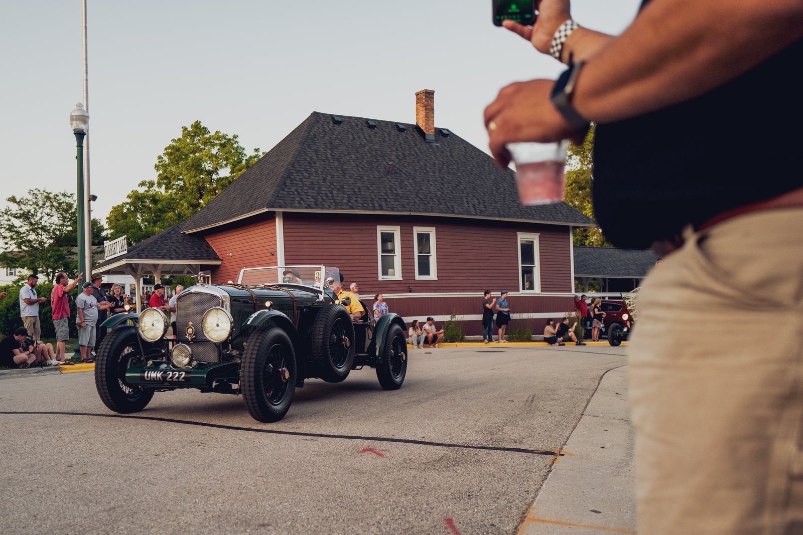Classic car driving past spectators at a street event, captured from a front 3/4 angle.