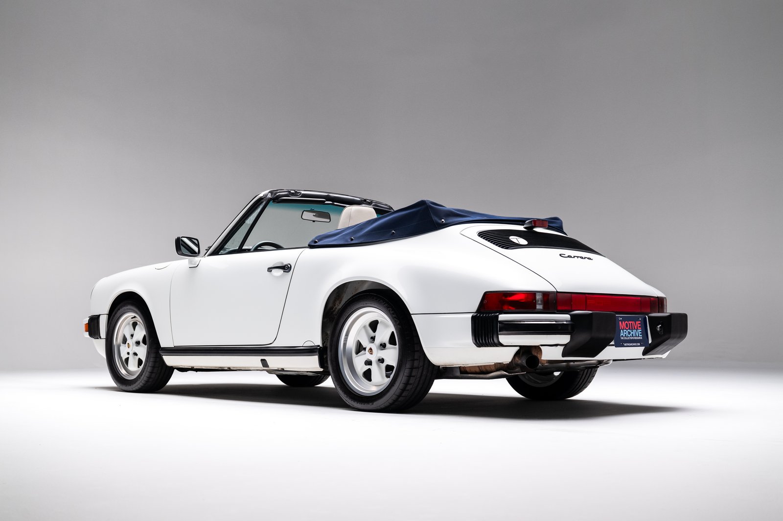 Rear three-quarter studio view of the 1988 Porsche 911 Carrera Cabriolet showing the rear light bar and folded soft top.