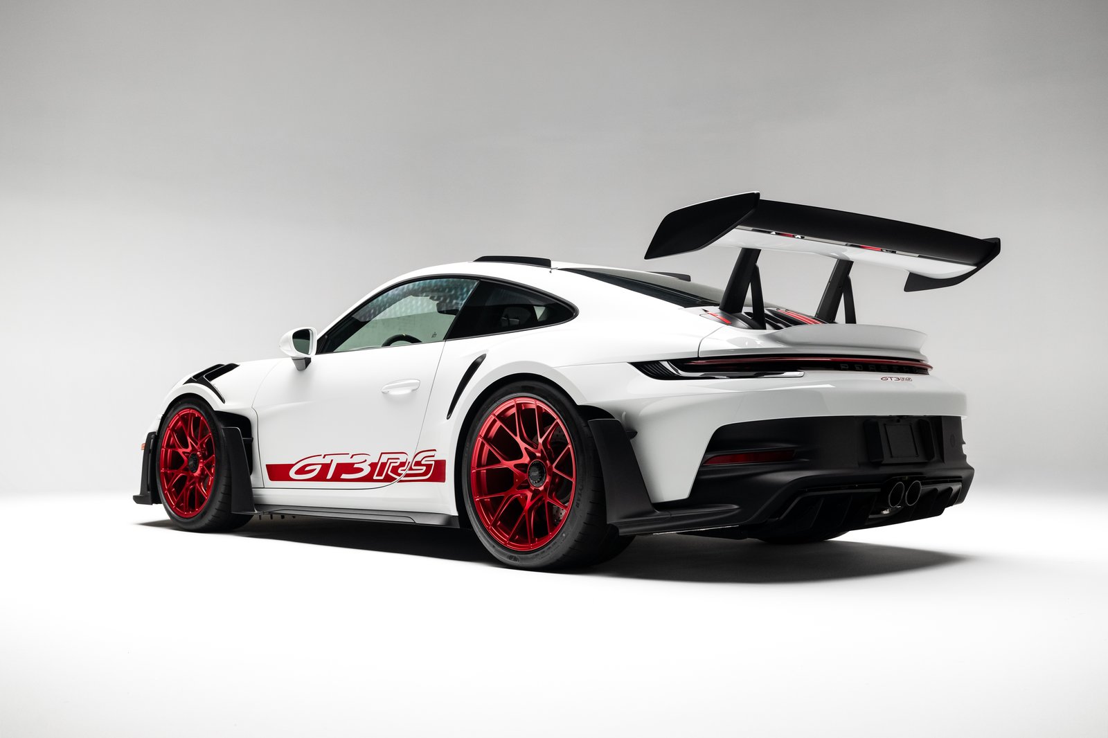 Rear three-quarter studio view of the 2023 Porsche 911 GT3 RS showing the swan-neck rear wing, red wheels, and wide rear bodywork.