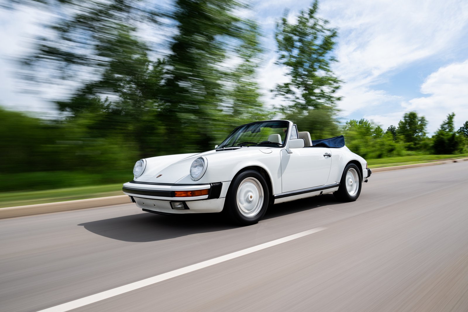 Rolling front three-quarter view of the 1988 Porsche 911 Carrera Cabriolet with the soft top down.