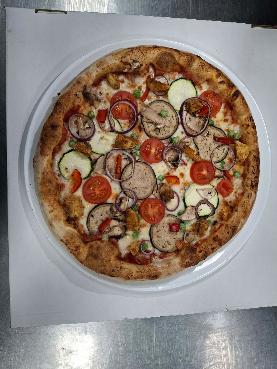 Pizza specjał tygodnia z kurczakiem, boczkiem i warzywami: cebula, cukinia, bakłażan, pomidorki i papryka w restauracji