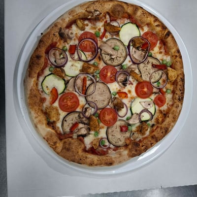 Pizza specjał tygodnia z kurczakiem, boczkiem i warzywami: cebula, cukinia, bakłażan, pomidorki i papryka w restauracji