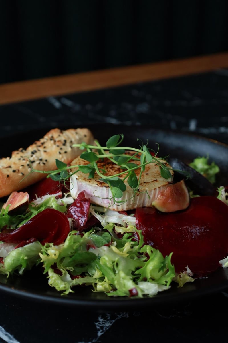 Sałatka z grillowanym kozim serem, figą i burakiem w restauracji, świeże sałaty, karmelizowana cebula i włoskie pieczywo