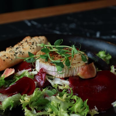 Sałatka z grillowanym kozim serem, figą i burakiem w restauracji, świeże sałaty, karmelizowana cebula i włoskie pieczywo