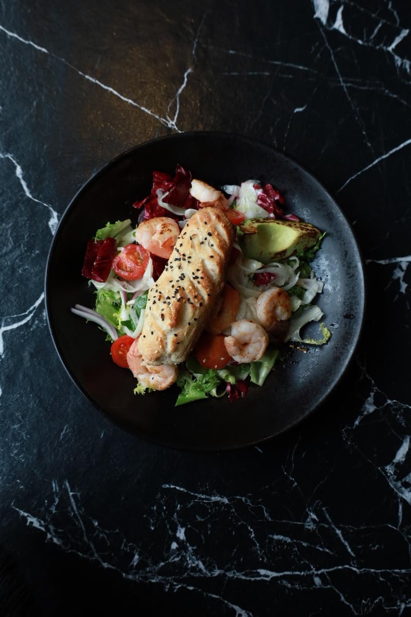 Sałatka z krewetkami królewskimi, grillowanym awokado i pomidorami cherry, świeża przystawka w restauracji z włoskim pieczywem