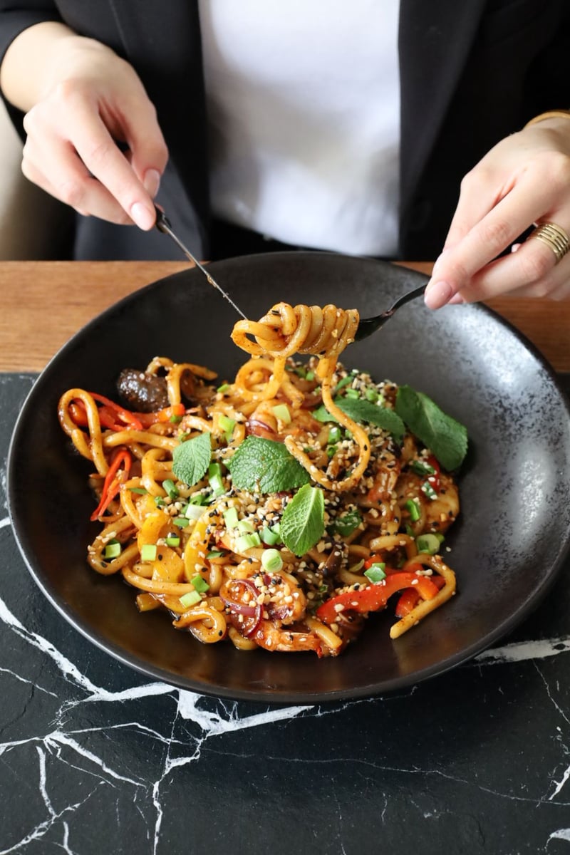 Makaron udon z papryką, cebulą, pędami bambusa i sosem teriyaki podany w restauracji azjatyckiej, idealny na obiad i kolację