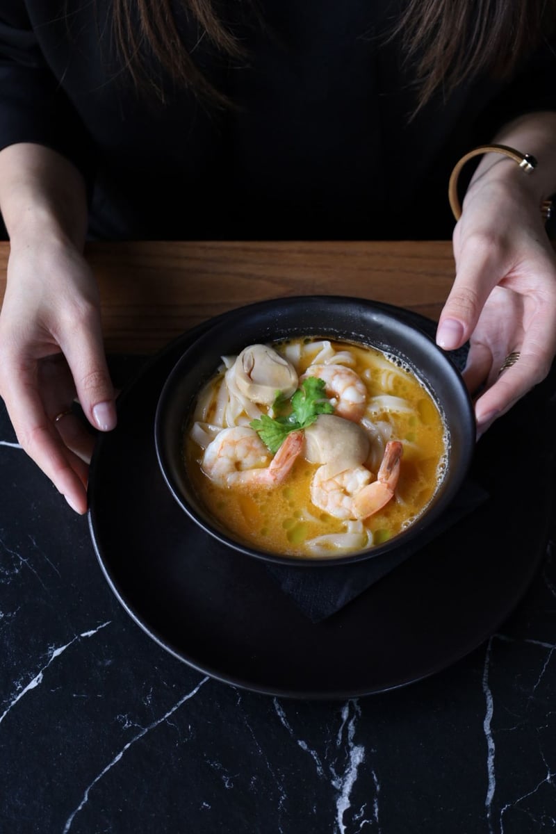 Tom Yum Kung z krewetkami, mleczkiem kokosowym, ziołami i makaronem ryżowym podany w restauracji azjatyckiej na eleganckim stole