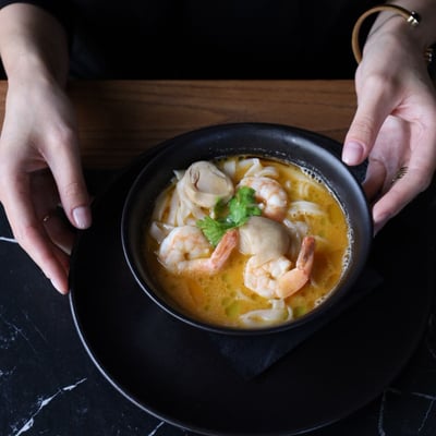 Tom Yum Kung z krewetkami, mleczkiem kokosowym, ziołami i makaronem ryżowym podany w restauracji azjatyckiej na eleganckim stole