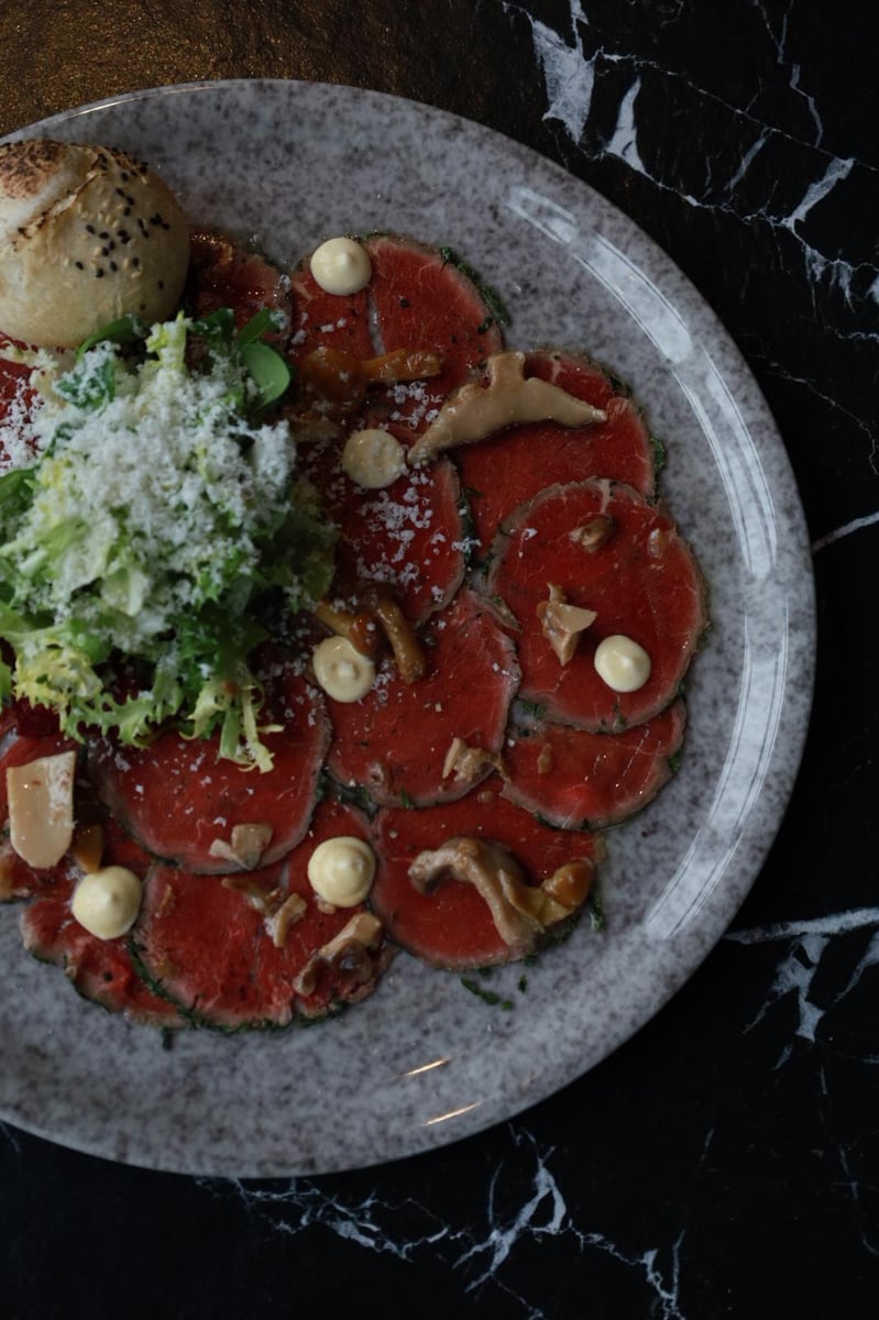 Carpaccio wołowe z parmezanem, mixem sałat, grzybami marynowanymi i włoskim pieczywem, eleganckie danie w restauracji włoskiej