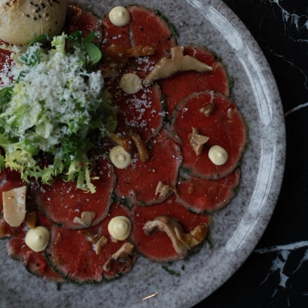 Carpaccio wołowe z parmezanem, mixem sałat, grzybami marynowanymi i włoskim pieczywem, eleganckie danie w restauracji włoskiej