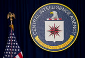 The seal of the CIA on a curtain next to an American flag.
