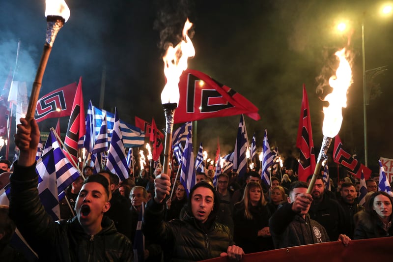 People rally with a torch, Greek flags and swastika banners.