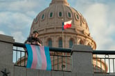 A person standing outside Texas Capitol with a Transgender pride flag