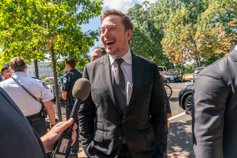 Elon Musk laughs while speaking to a reporter.
