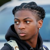 A Black male teenager with twisted dreadlocks walks by a vehicle.