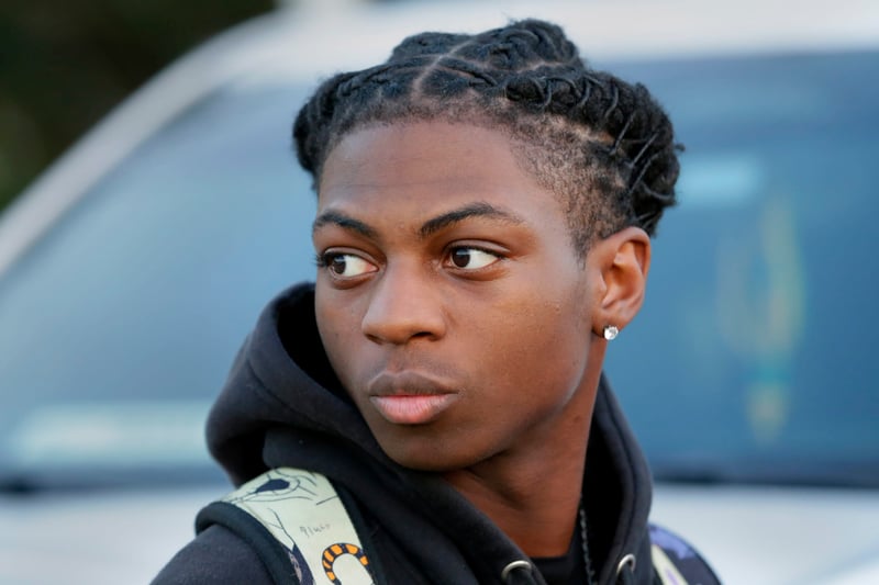 A Black male teenager with twisted dreadlocks walks by a vehicle.