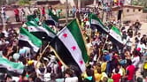 Protesters gather during a demonstration in Daraa, Syria, with some of them carrying Syrian revolutionary flags.