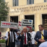 Peter Navarro speaking outside the D.C. federal courthouse with protestors holding supportive and critical signs behind him.