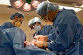 Three surgeons in personal protective equipment perform a bilateral mastectomy.