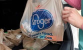 A person takes a Kroger plastic bag out of their vehicle's trunk.