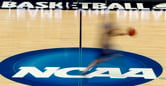 A blurry player on a basketball court with ball in hand and NCAA visible in the center.