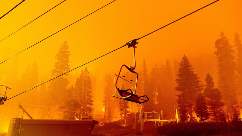 This photo shows the chair of a ski lift in the foreground with a forest fire raging behind.