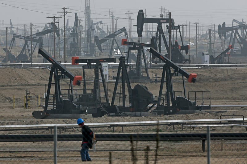 A person walks past pump jacks operating at the Kern River Oil Field in Bakersfield, Calif.