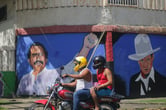 A motorcyclist rides past a mural of Daniel Ortega and Cesar Augusto Sandino in Nicaragua.