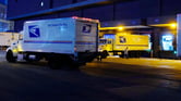 USPS delivery trucks arrive at a loading dock.