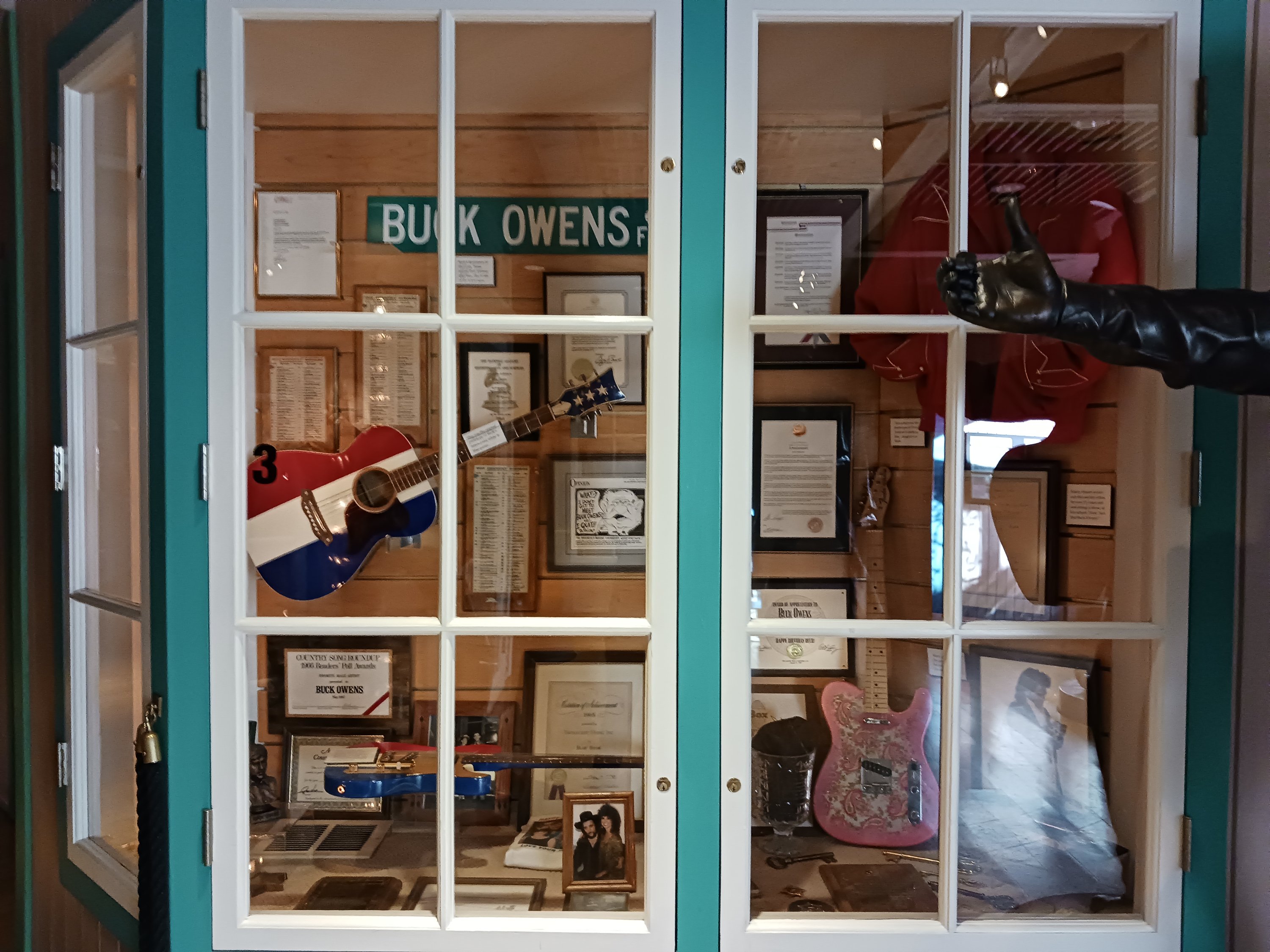 A glass display case featuring Buck Owens's red, white, and blue guitar, among other pieces of Classic Country memorabilia.
