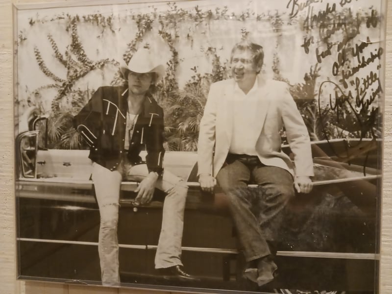 A black and white photograph featuring Dwight Yoakum and Buck Owens sitting together. A message from Dwight to Buck is scribbled in the top right corner.