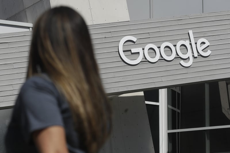 A woman walks below a Google sign on its campus in Mountain View, Calif.