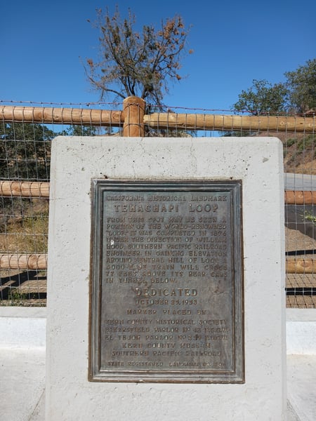 The dedication plaque erected in 1953, when the Loop was designated a California Historical Landmark. The metal plaque is surrounded by a concrete frame. The words are weathered and worn with age, but still readable.