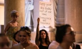 Demonstrators gather inside the Indiana Statehouse, with one holding a sign.