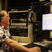 A radio DJ reads the news off of a computer screen in a radio studio.
