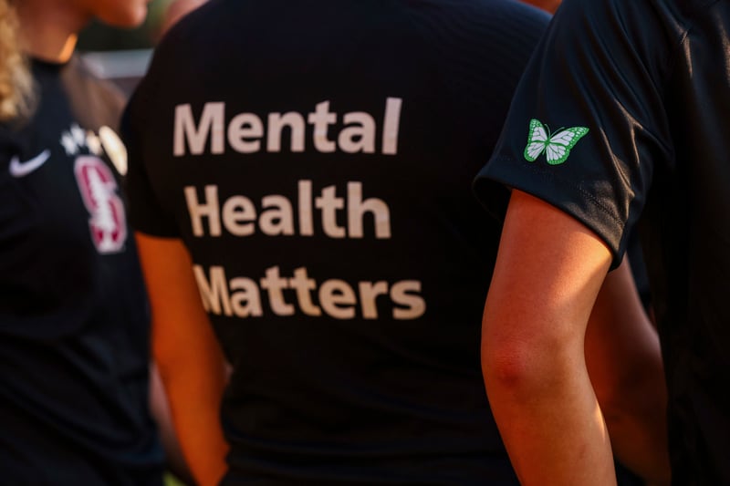 Two women stand on either side of a woman wearing a shirt that reads "Mental Health Matters" on the back.