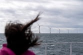 A person on a boat stands in front of five offshore wind turbines.